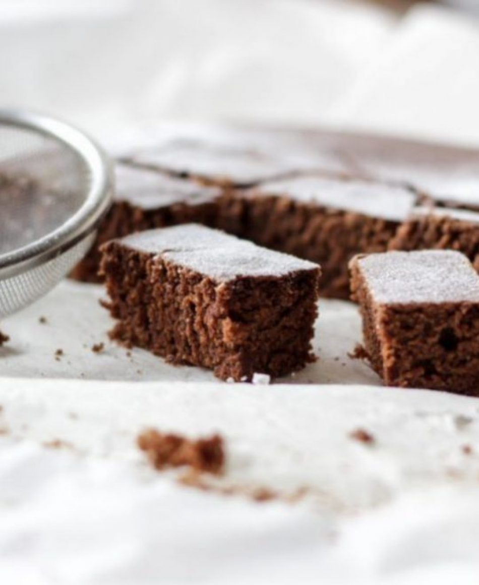 Foto de diversos pedaços de um bolo, que aparenta ser de chocolate, com uma peneira ao lado.