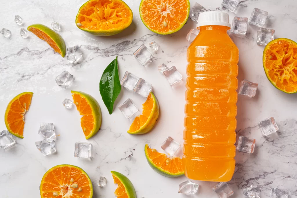 um copo de suco de laranja e frutas frescas no chao com cubos de gelo 1