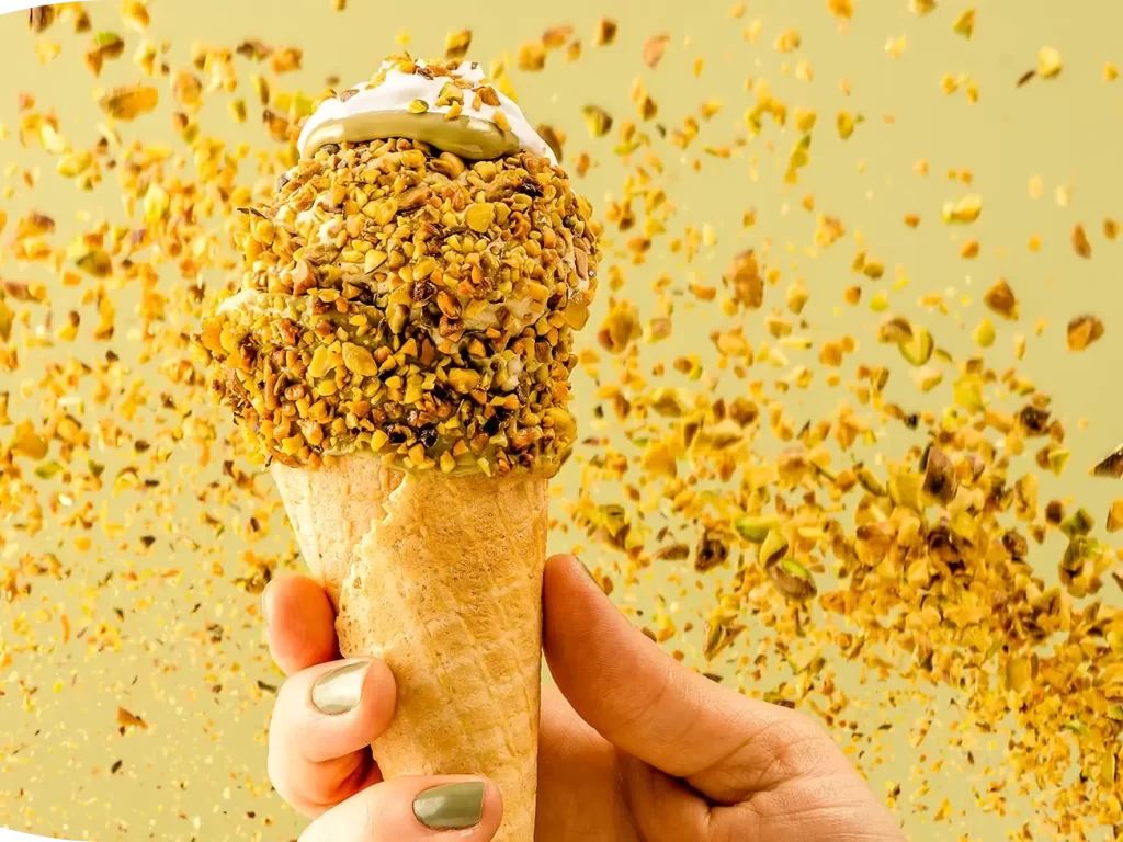 Casquinha de sorvete de pistache com grãos de pistache envolta do sorvete e voando ao fundo