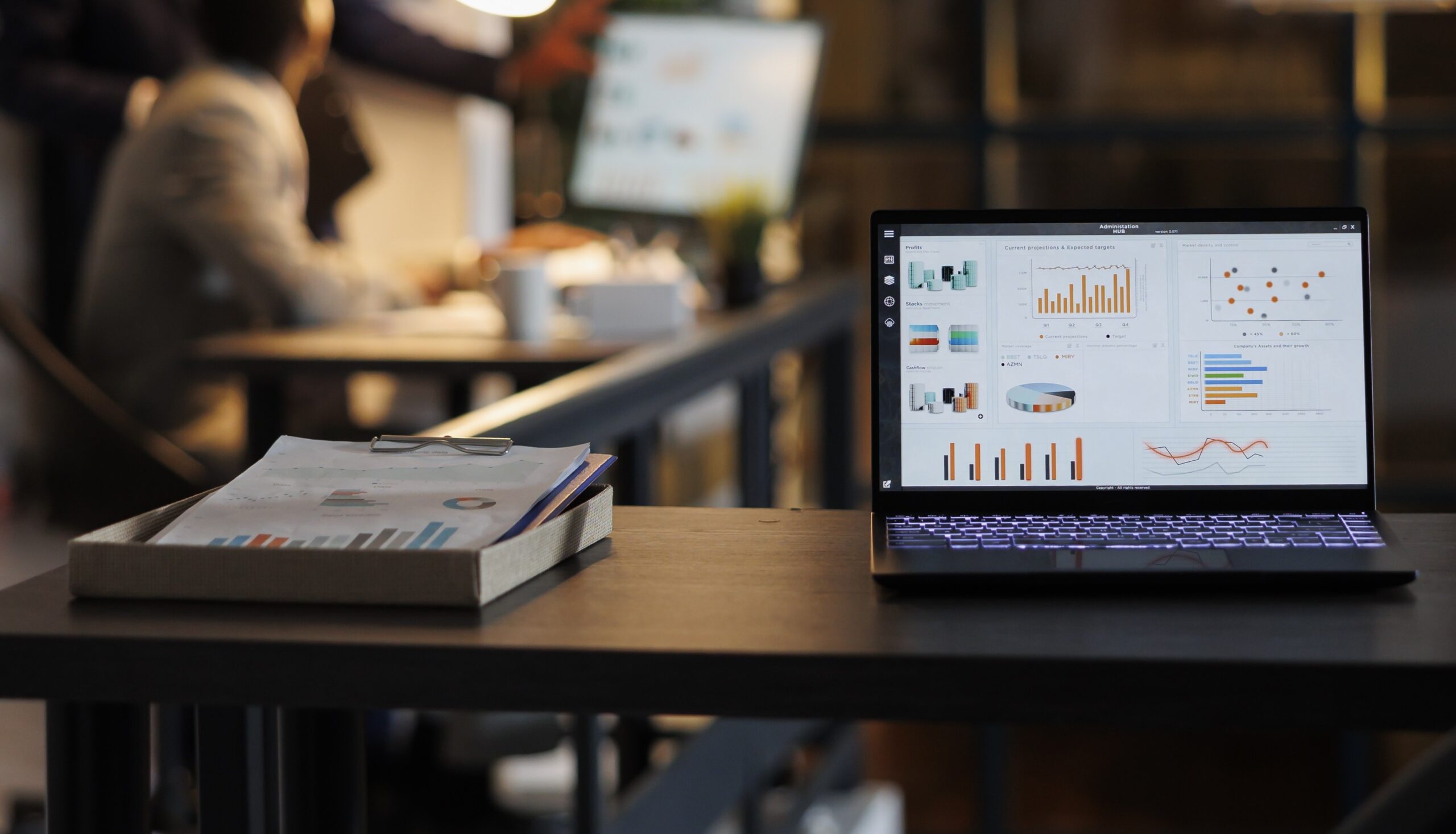 laptop computer with financial graphs screen standing table startup office coworkers discussing company strategy background employees working late night startup office 2 scaled